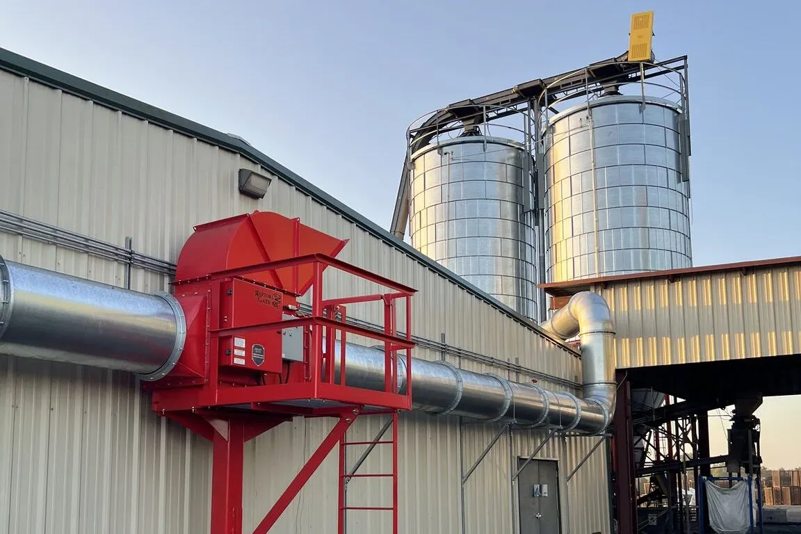 A red abort gate on insulated ducting mounted to a plant wall, with grain silos behind.