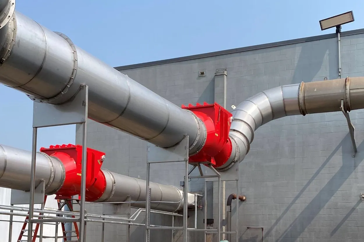 Two red abort gates on large-diameter outdoor ducting carried on steel supports.