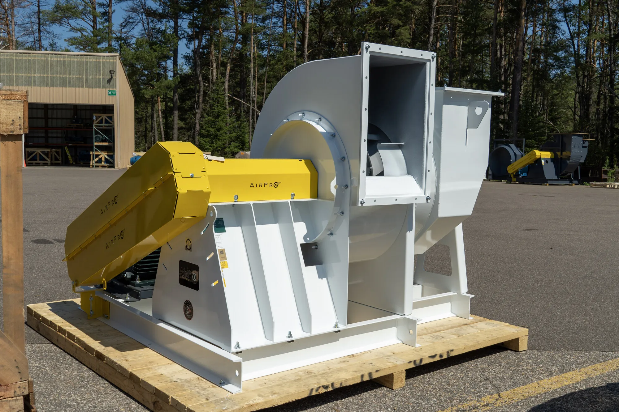 A white and yellow AirPro industrial centrifugal fan, crated on a shipping pallet outside the factory.