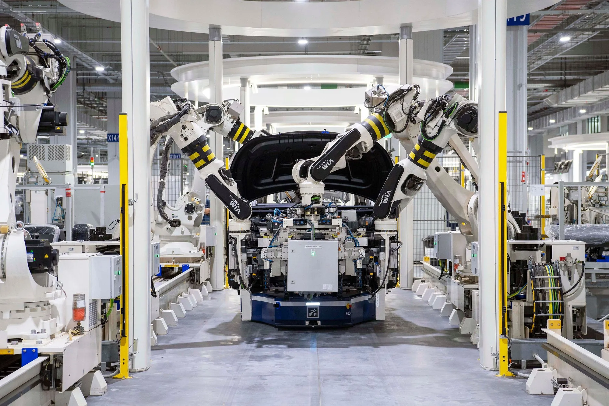 Robot arms working over a car body on an automotive assembly line in a bright factory.