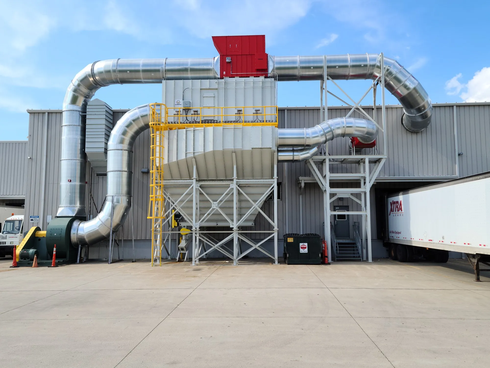 A large fabric-filter collector with a red hopper and insulated ducting outside a plant, beside a loading dock.