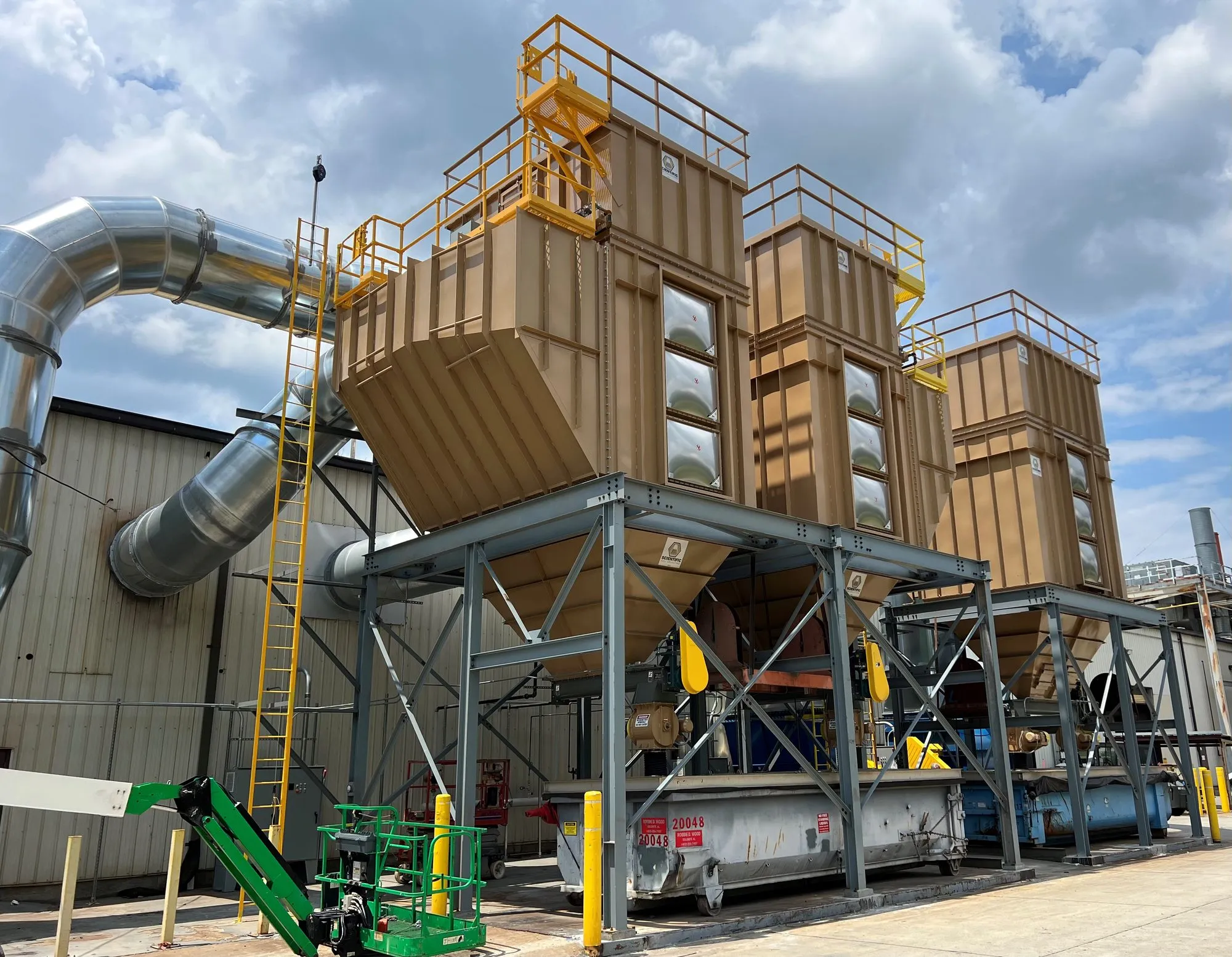 A multi-module baghouse on structural steel outdoors, with access platforms, caged ladder and inlet ducting.