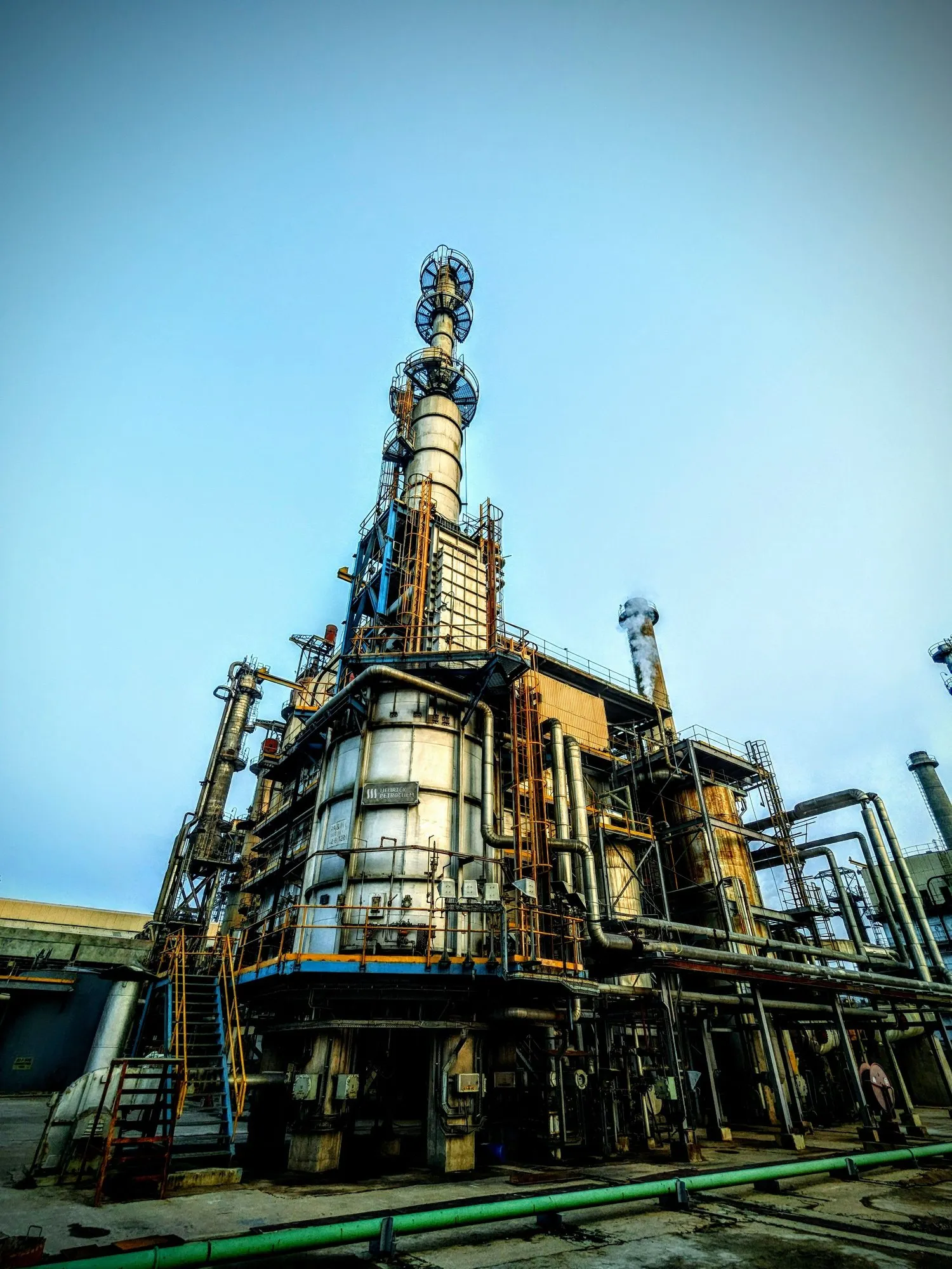 A chemical processing tower and its pipework against a clear sky.
