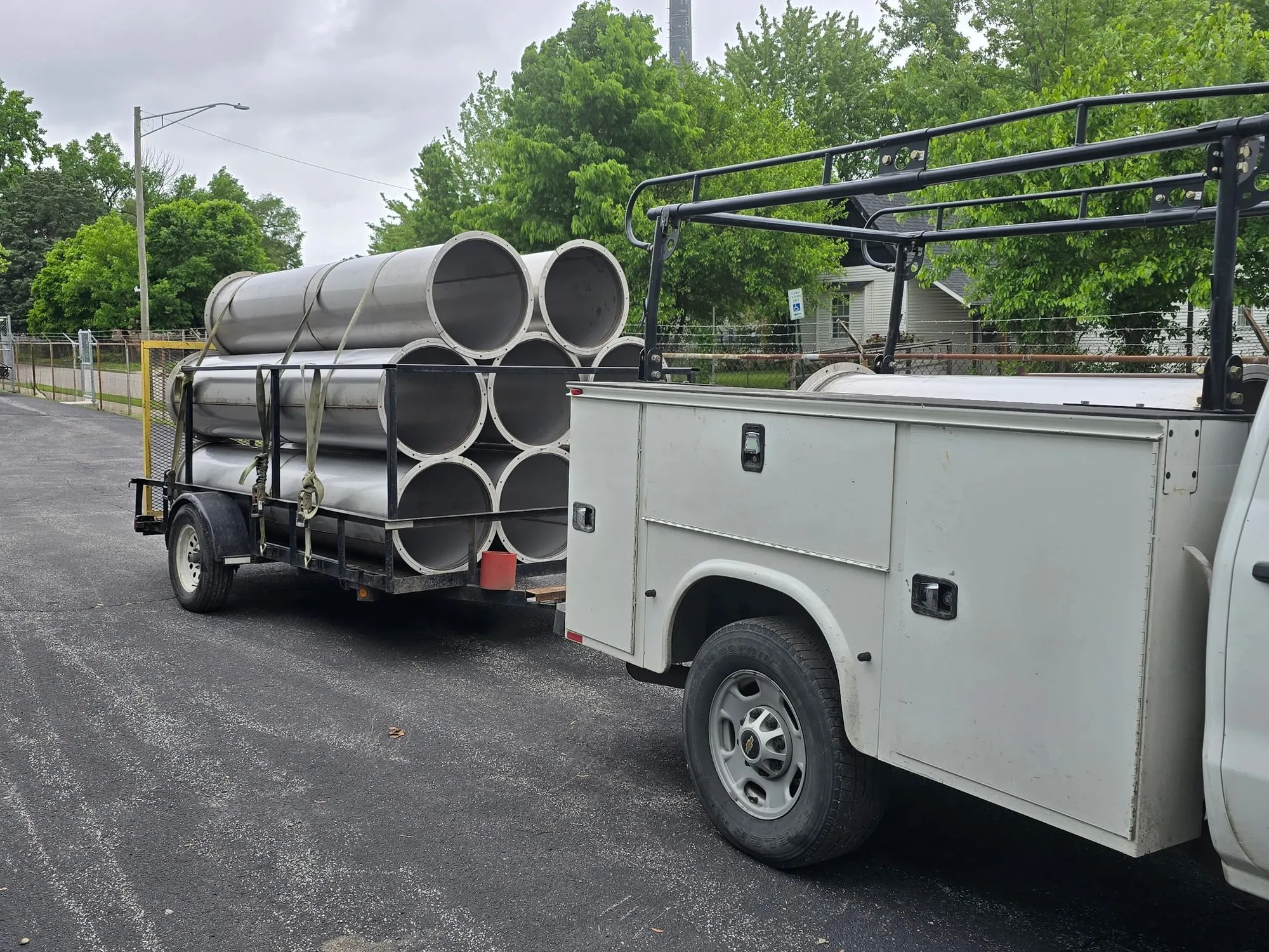 Lengths of large-diameter spiral duct strapped to a trailer behind a white service truck.