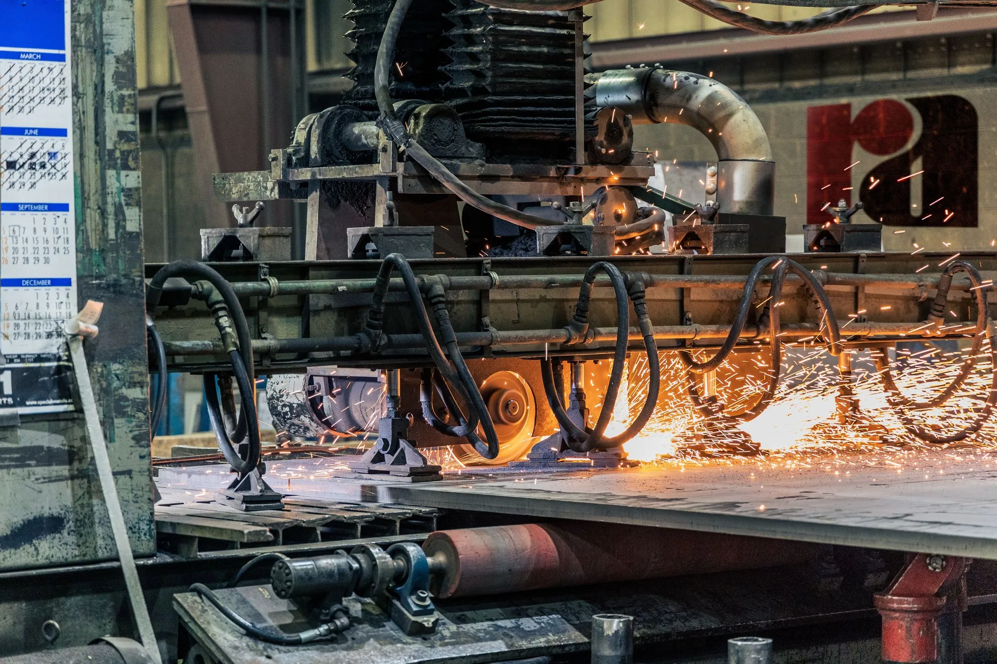 Industrial machinery grinding a metal workpiece on a production line, sparks streaming across the bed.
